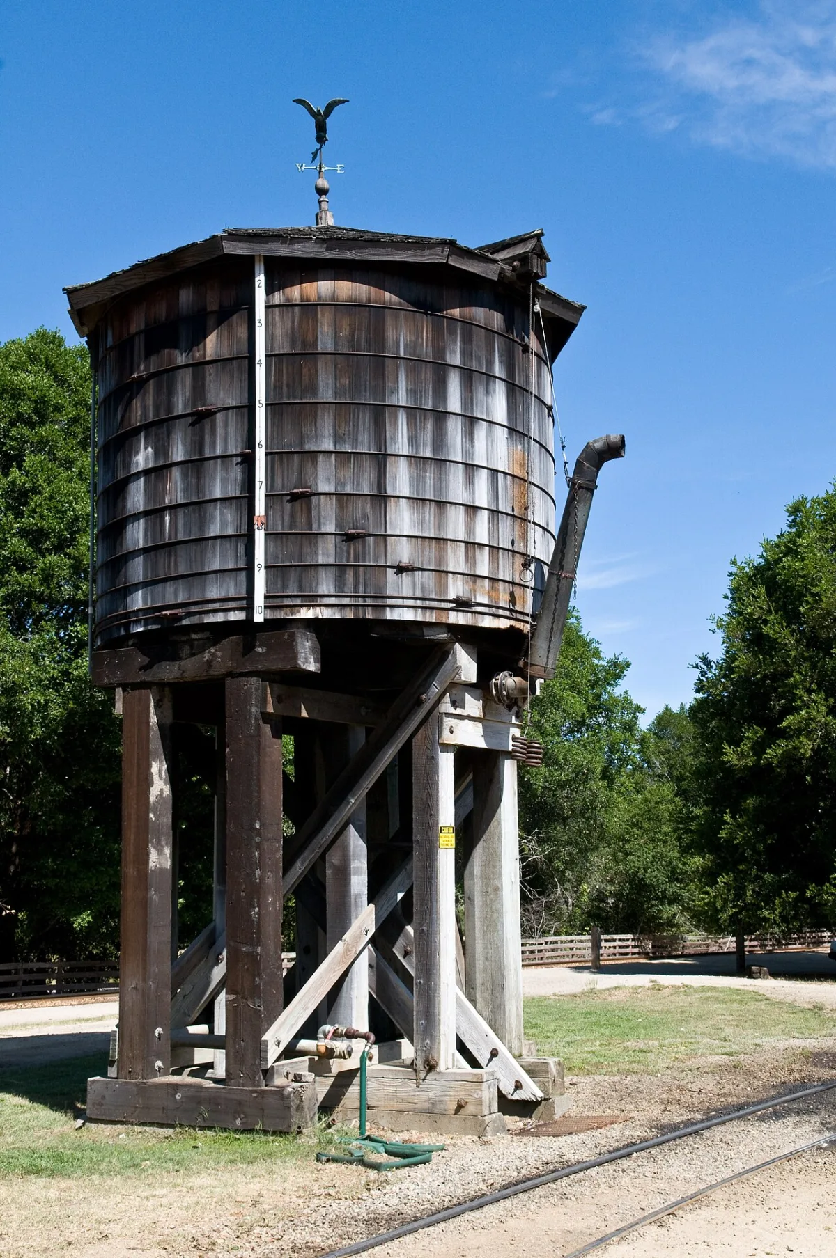 Houten watertoren op stellage bij een spoorlijn, met windvaan op het dak